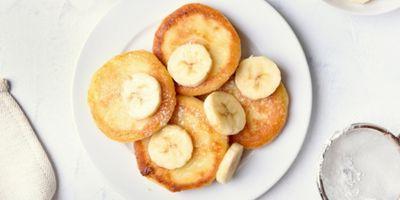 Four cottage cheese pancakes on a white plate garnished with banana slices and powdered sugar,